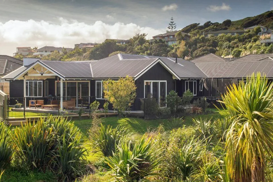 Finished new build with dark weatherboard cladding, a covered gable porch and native planting in front